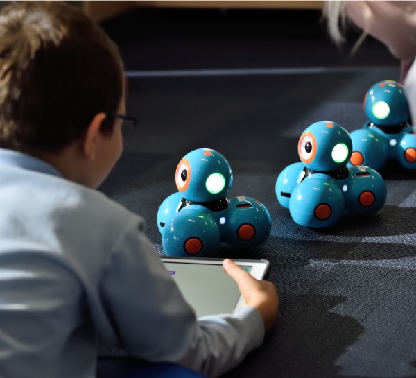 A child sitting on the floor, using a tablet to control a small robot.