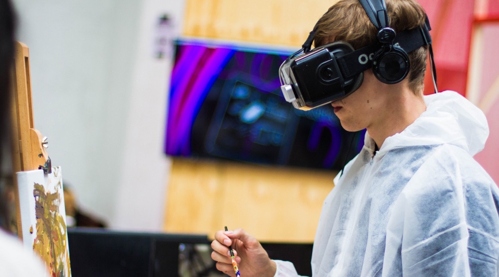 A young man painting, while wearing an augmented reality headset and headphones.