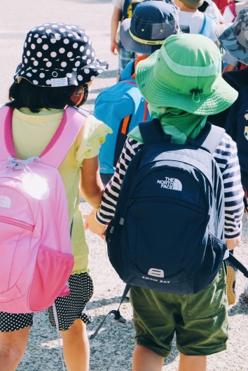 Two children wearing sunhats and backpacks, while holding hands and walking together.